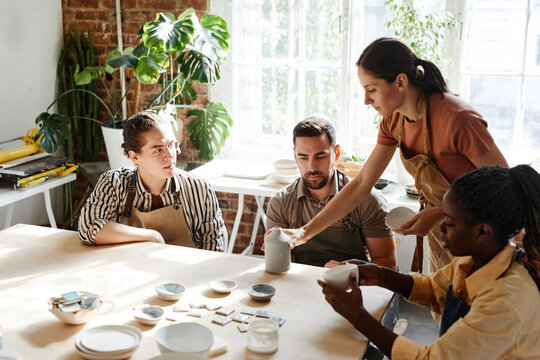 Warm toned portrait of diverse group of people enjoying pottery class in cozy studio