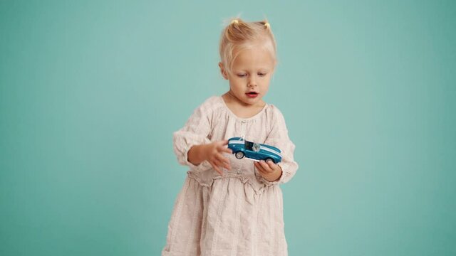Concentrated girl playing with car in blue studio