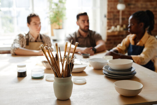 Warm toned portrait of diverse group of people enjoying pottery class in cozy studio, focus on foreground, copy space - Powered by Adobe