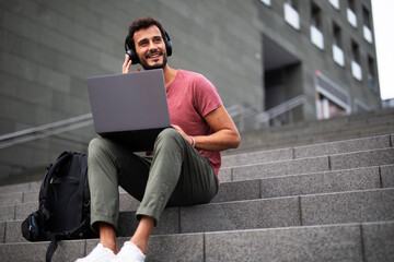 Handsome man working with laptop on city street. Man using his laptop while sitting on stairs...