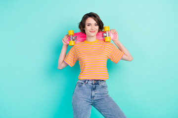 Photo of pretty funky young woman dressed striped t-shirt smiling holding skateboard isolated teal color background