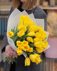 Beautiful yellow tulips bouquet. Young woman holding big bouquet of fresh tulips wrapped in paper.