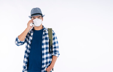 Lifestyle travel new normal safety concept. Traveler young man wear shirt, hat and face mask with backpack protect outbreak talking with smartphone while standing over isolated white background.