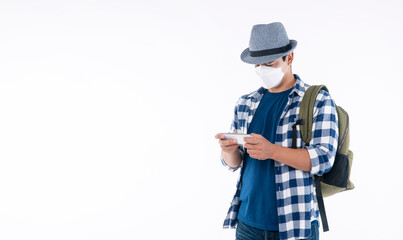 Lifestyle travel new normal safety concept. Traveler young man wear shirt, hat and face mask with backpack protect outbreak while looking map in smartphone standing over isolated white background.