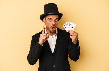 Young caucasian wizard holding magic card isolated on yellow background having an idea, inspiration concept.