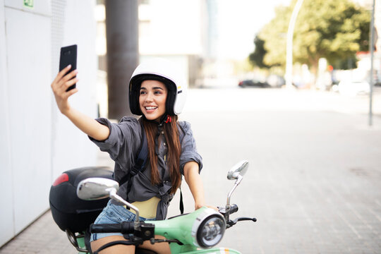 Beautiful woman getting ready for a ride on scooter. Beautiful happy lady taking selfie photo.