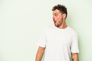 Young caucasian man isolated on green background being shocked because of something she has seen.