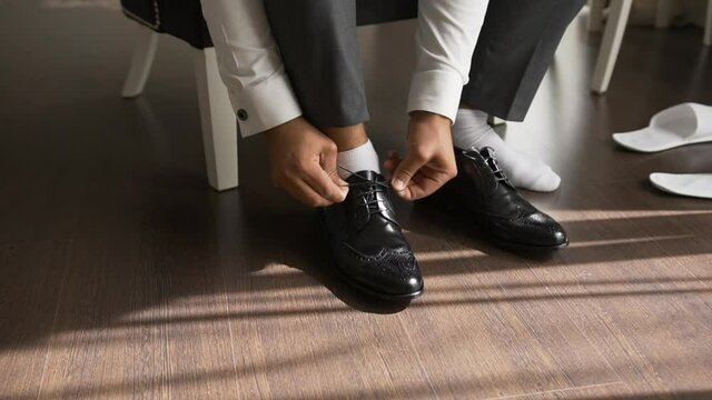 An elegantly dressed man puts on shoes and ties the laces on patent leather shoes with lace. Classic fashionable shoes. Modern men's shoes.