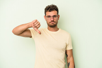 Young caucasian man isolated on green background showing a dislike gesture, thumbs down....
