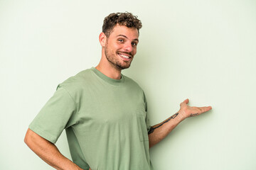 Young caucasian man isolated on green background showing a welcome expression.