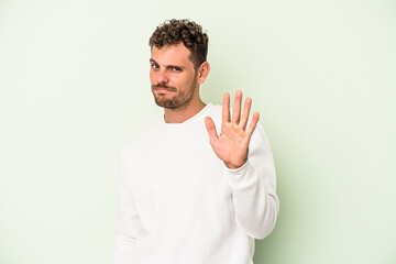 Young caucasian man isolated on green background rejecting someone showing a gesture of disgust.