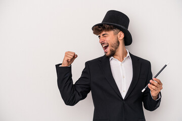 Young arab wizard man holding a wand isolated on white background raising fist after a victory,...