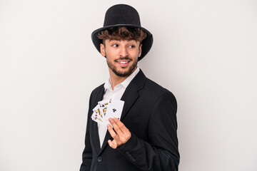 Young arab wizard man holding a magic cards isolated on white background looks aside smiling,...