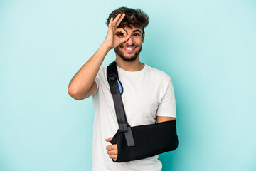 Young arab man with broken hand isolated on blue background excited keeping ok gesture on eye.
