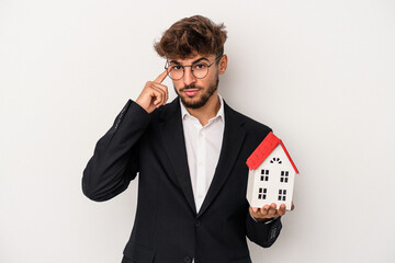 Young arab real estate man holding a model house isolated on isolated background pointing temple...
