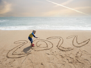 a child playing and writing on sand of seashore