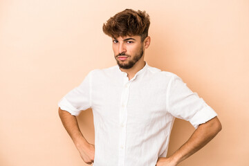 Young arab man isolated on beige background frowning face in displeasure, keeps arms folded.