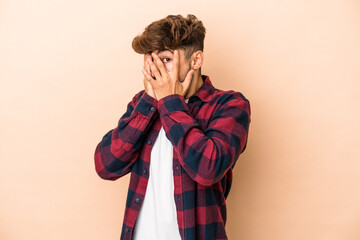 Young arab man isolated on beige background blink through fingers frightened and nervous.