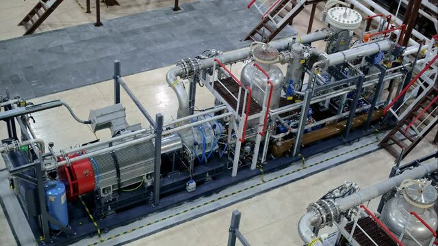 Working in the oil and gas industry, a worker in a helmet repairs and maintains a compressor unit for compressing natural gas. Screw compressor with electric motor and liquid cooling system.