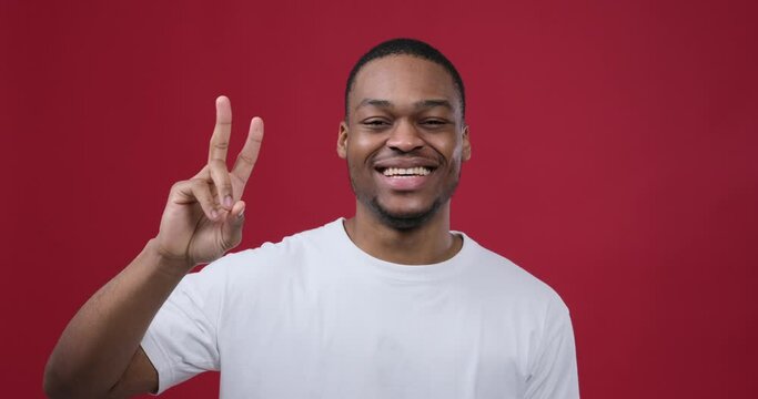 Joyful man giving v hand sign over maroon background