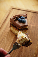 Piece of Kiev cake with chocolate icing and blueberries on wooden board. A bite of cake on a fork