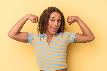 Young latin transsexual woman isolated on yellow background showing strength gesture with arms, symbol of feminine power