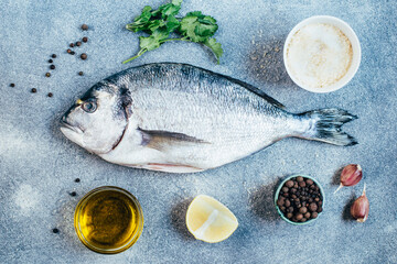 top view of raw dorado fish lemon pepper seasoning greens parsley garlic on gray background