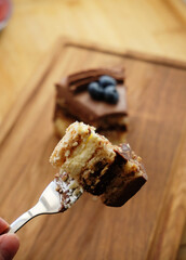 Piece of Kiev cake with chocolate icing and blueberries on wooden board. A bite of cake on a fork