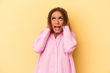 Young latin transsexual woman isolated on yellow background covering ears with hands trying not to hear too loud sound.