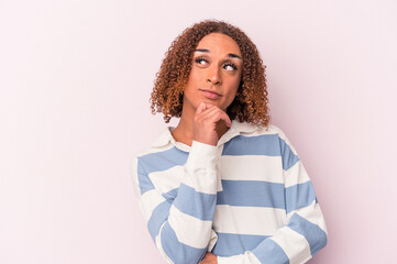 Young latin transsexual woman isolated on pink background relaxed thinking about something looking at a copy space.