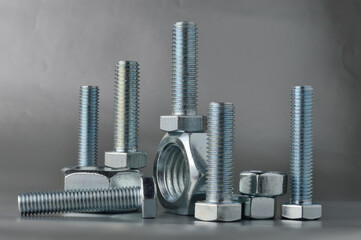 composition of new bolts and nuts of different sizes on a gray background.