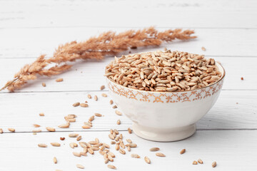 A pile of rye grains, in a white porcelain plate on a light background. Spikelet
