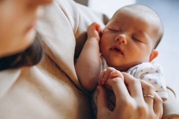 close up portrait of a beautiful sleeping baby in the arms of mom in the bedroom in daylight