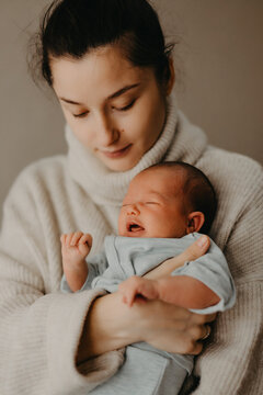 Loving mother carying of her newborn baby at home. Bright portrait of happy mum holding cute infant child on hands. Mother hugging her little 1 months old daughter.