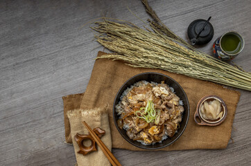 Japanese pork rice bowl with egg and onion (Donburi) served with pickled ginger and green tea on wooden table. Japanese food style. Top view.