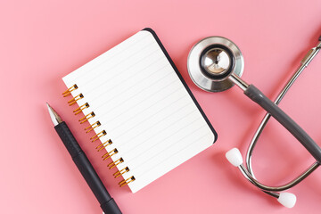 Notebook and pen with stethoscope on pink background. equipment business hospital. work and care concept.