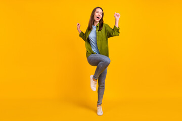 Photo of sweet lucky young lady wear green shirt smiling rising fists isolated yellow color background