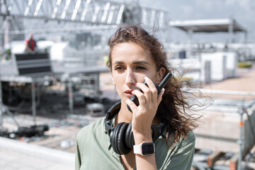 Installation of stage equipment and preparing for a live concert open air. Event manager portrait. Summer music city festival. Young serious woman speaks the walkie-talkie. - 466490442