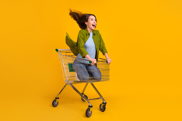 Full size photo of happy nice young woman look empty space ride trolley isolated on yellow color...