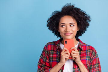 Photo of young afro girl happy positive smile think dream smartphone touch chin isolated over blue color background