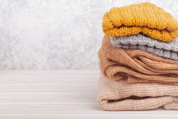 Pile of warm knitted clothes, sweaters and caps on rustic white wooden background. Cozy folded knitwear stack, winter wardrobe capsule concept, shopping, free space for text