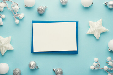 Top view photo of paper sheet on blue envelope white and silver christmas tree decorations stars balls and snowy branches on isolated pastel blue background with empty space