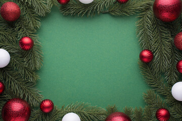 Top view photo of red and white christmas tree balls on pine branches on isolated green background with copyspace in the middle