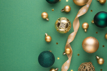 Top view photo of gold and green christmas tree decorations balls ribbon serpentine and stars confetti on isolated green background with copyspace