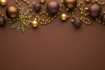 Top view photo of golden and brown christmas tree balls snowflake and gold beard garland on isolated brown background with blank space