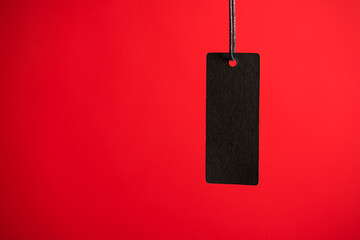 Photo of hanging black price tag on isolated red background with blank space