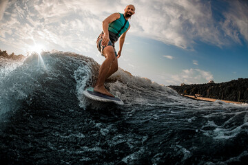 Fototapeta na wymiar Happy active man wakesurfing on a board down the blue water on summer day