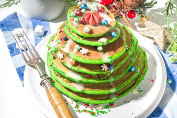 Stack of green colored breakfast pancakes, like Christmas tree with sugar sprinkles. Festive Christmas breakfast on Xmas and New Year decorated table