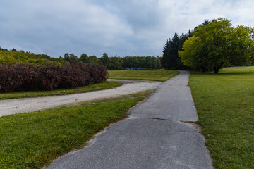 Long asphalt path in Citadel park with trees and lamps around next to big green glade