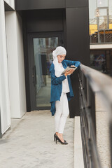 Portrait of an Arab student girl holding a tablet. Arab business woman in hijab holding a tablet in the street. Woman is dressed in hijab